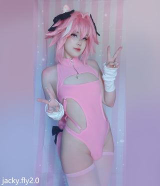 A person posing in a pink bodysuit with cutouts, pink hair, and white arm wraps, standing against a pink striped backdrop. The watermark 'jacky