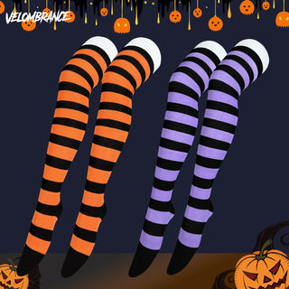 Four Halloween-themed striped leg warmers or socks displayed on invisible legs against a dark navy background with pumpkin decorations. Two pairs are orange and black striped, and two pairs are purple and black striped.